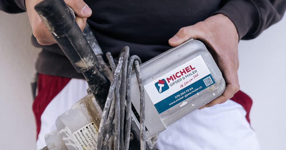 Handwerker hält eine professionelle Verputzmaschine mit dem Logo der Firma Michel Gipser und Maler.